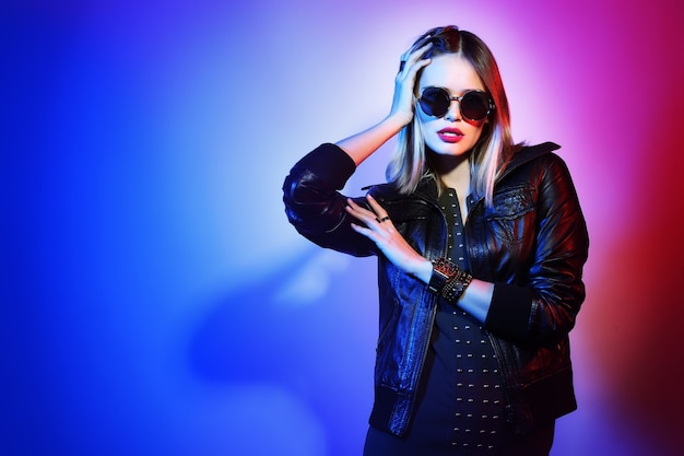 Fashion portrait of young elegant woman in sunglasses. Black leather jacket, colored background, studio shot