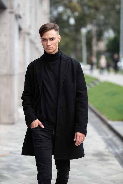 Fashion portrait of a young guy in black clothes of model appearance on the street