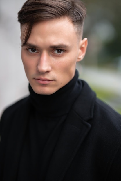 Fashion portrait of a young guy in black clothes of model appearance on the street