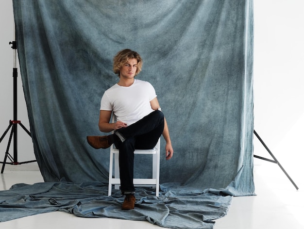 Photo fashion portrait of young man in white shirt poses in studio over blue background