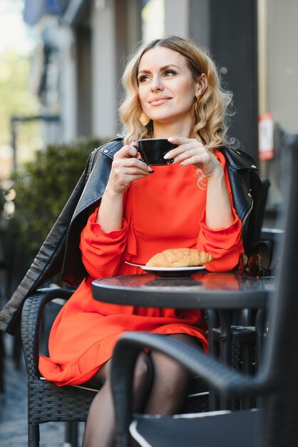 Fashion portrait of young woman siting at the table with cup of coffee, tea in street cafe.