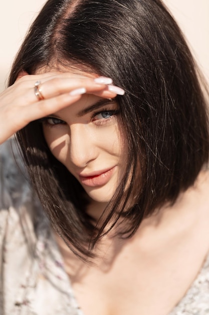 Fashion pretty young woman mode with hairstyle in stylish dress sits coverts her amazing blue eyes and looks at the camera in sunny summer day