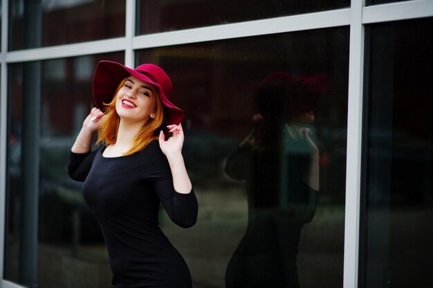 Fashion red haired girl on pink hat and black dress with bright make on large window