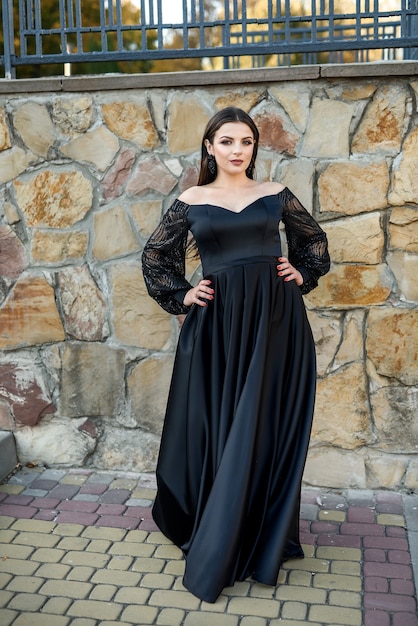 Fashion smiling woman in black dress on a brick background. Fashion