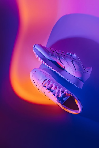 Fashion  sneakers on vivid abstract background. Sport shoes in neon light. Violet and orange gradient.