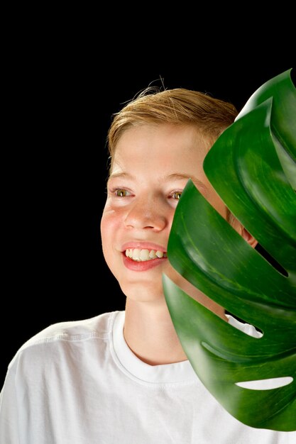 Fashion studio portrait of a boy holds green monstera leaf cosmetology concept for young teenagers