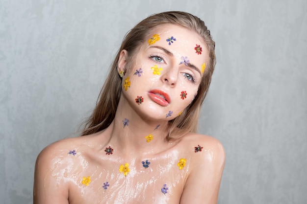 Fashion studio portrait of nude elegant lady with flowers and transparent gel on her face. Body and skin care, perfume, cosmetic concept.