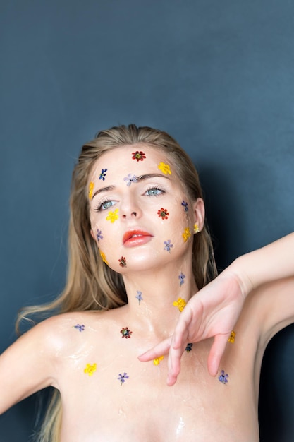 Fashion studio portrait of nude elegant lady with flowers and transparent gel on her face. Body and skin care, perfume, cosmetic concept.