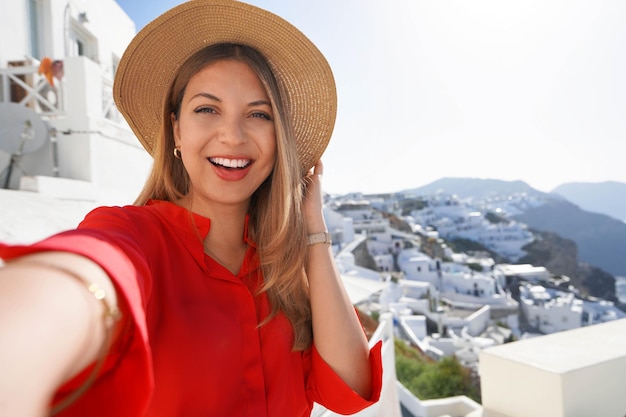 Fashion traveler girl taking selfie photo in Oia picturesque greek village of Santorini Island Young woman enjoying holidays in Greece Europe