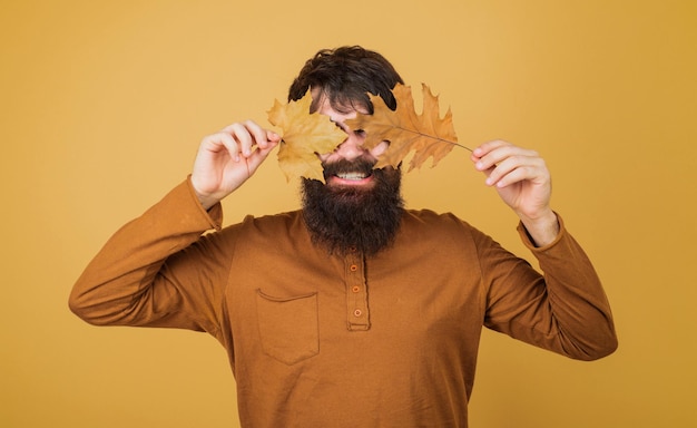 Photo fashion trends for fall smiling autumn man covered eyes with autumnal foliage handsome man in orange