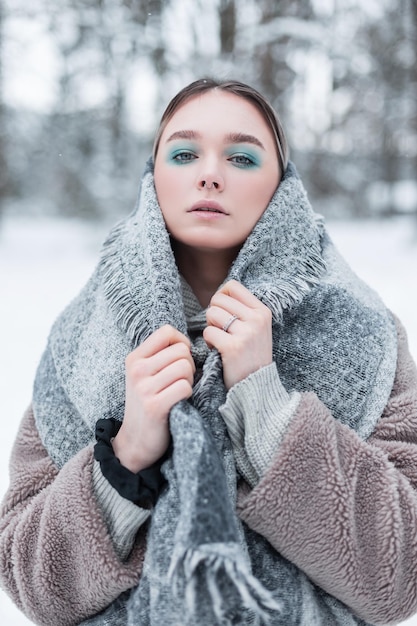 Fashion vogue russian girl model in make-up with a vintage scarf and a fur coat on a cold winter day with snow in nature