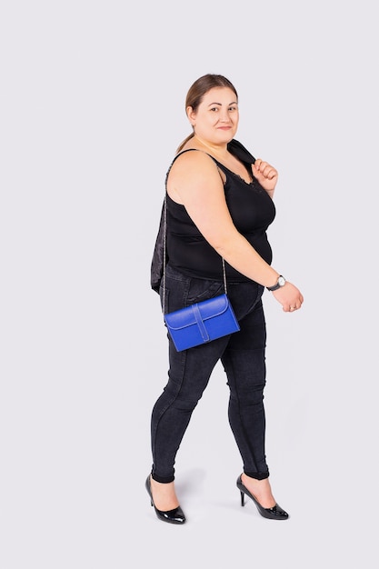 Fashion woman in a good mood dressing in a black jeans and shirt holding a blue bag on a right arm isolated on grey background