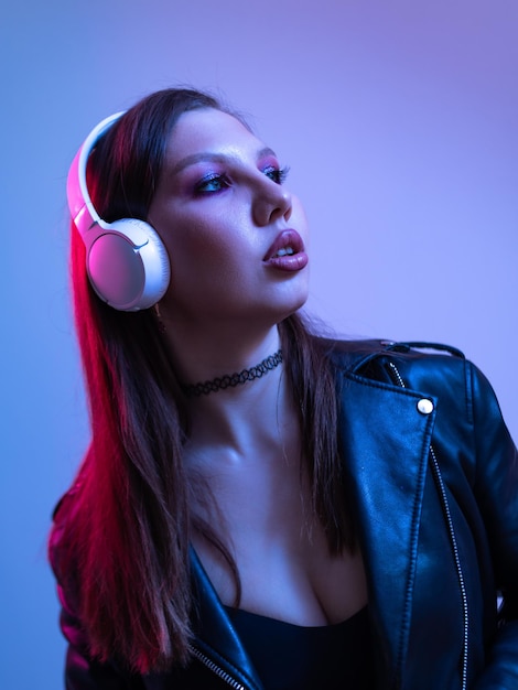 Fashion woman with headphones listening to music over neon background at studio