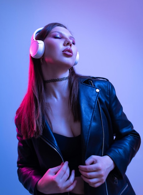 Fashion woman with headphones listening to music over neon background at studio