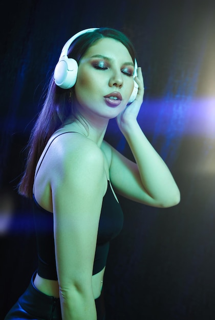 Fashion woman with headphones listening to music over neon background at studio