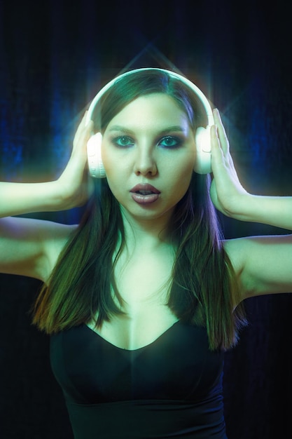 Fashion woman with headphones listening to music over neon background at studio