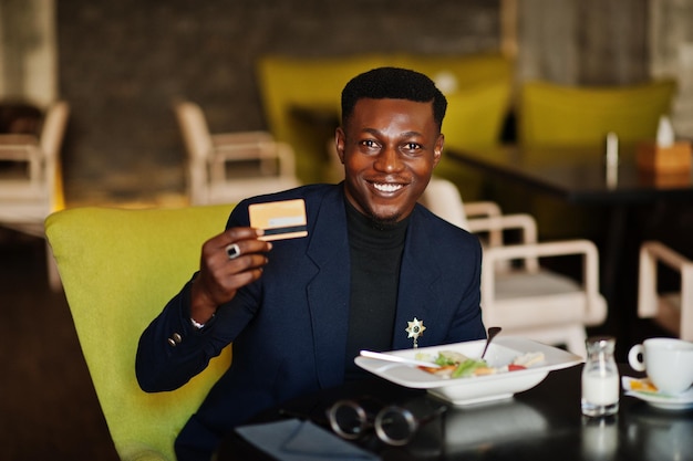 Fashionable african american man in suit sitting at cafe with credit card in his hand