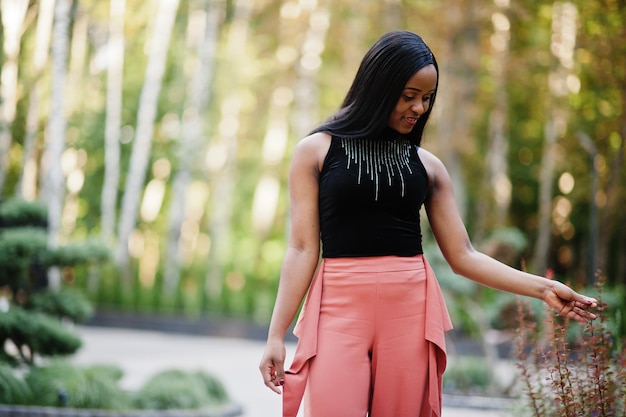 Fashionable african american woman in peach pants and black blouse pose outdoor.