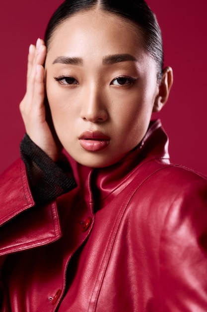 Photo fashionable asian woman with brunette hair wearing a red leather jacket posing against a red