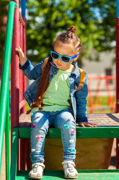 Fashionable baby girl in sunglasses. in a denim suit in the park in summer