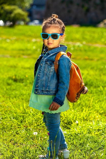 Fashionable baby girl in sunglasses. in a denim suit in the park in summer