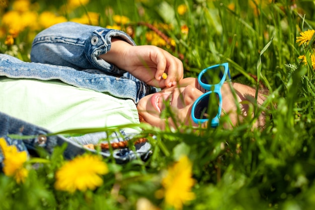 Fashionable baby girl in sunglasses lies on the grass in the park in summer