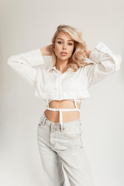 Fashionable beautiful stylish elegant girl model in a fashionable white shirt and stylish jeans with a high waist in the studio on a white background