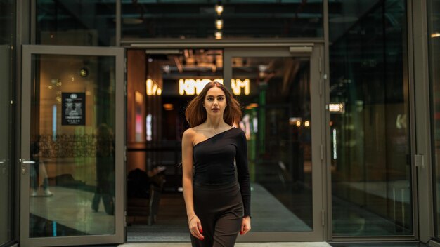 Fashionable beautiful woman model in black stylish clothes with trousers and a black oneshoulder top walks in office building