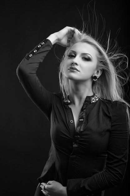 Fashionable blond woman with perfect makeup and hair in wind wears blouse, posing at studio. Black and white shot