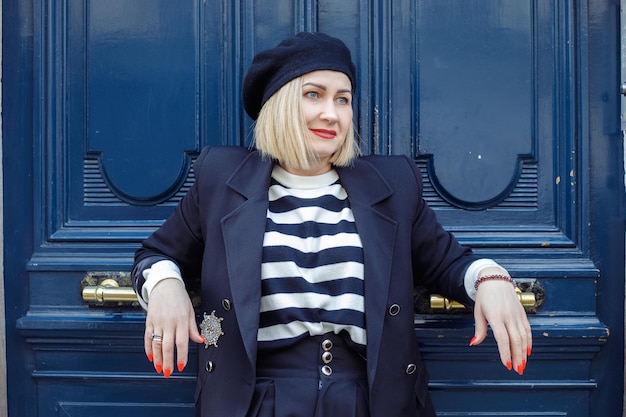 Fashionable blonde with square hairstyle is leaning against bright blue door in old part of city