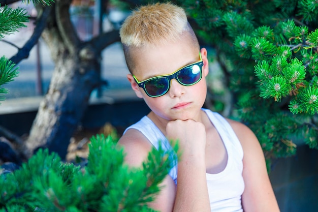 Photo fashionable boy in dark glasses sits at a table in a cafe. around a pine branch