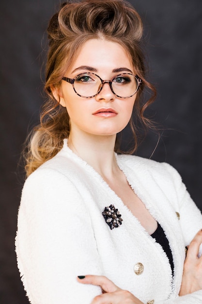 Fashionable brunette girl posing on a black background in a stylish white jacket and glasses