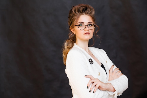 Fashionable brunette girl posing on a black background in a stylish white jacket and glasses