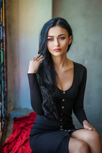 Fashionable brunette woman in black dress sitting near the stained glass window