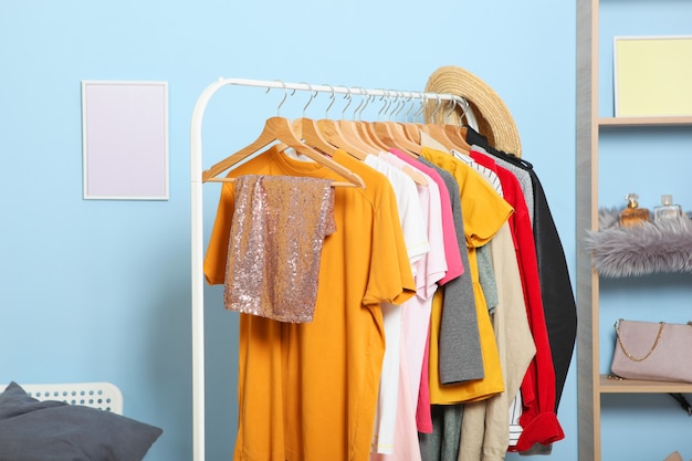 Fashionable clothes on hangers on a wardrobe rack on a colored background