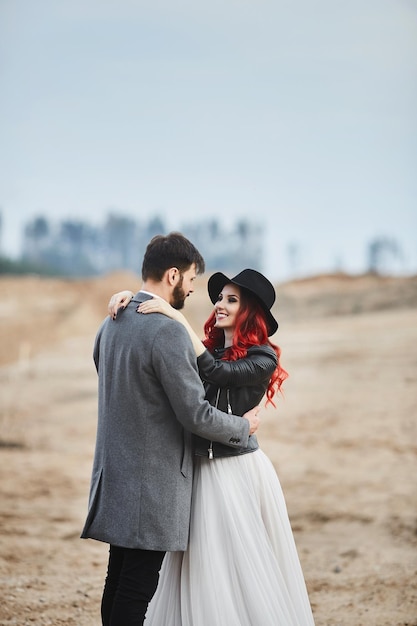 A fashionable couple of newlyweds posing outdoors stylish bearded man and his redhaired girlfriend i...