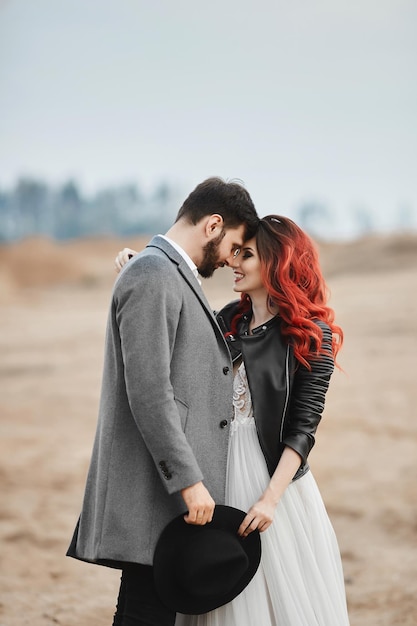 A fashionable couple of newlyweds posing outdoors stylish bearded man and his redhaired girlfriend i...