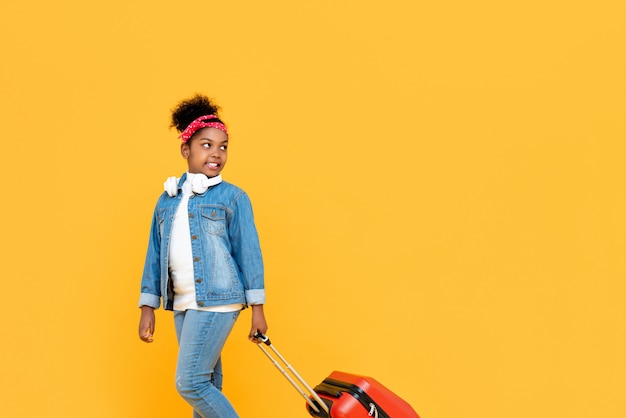 Fashionable cute African girl with luggage ready to travel isolated on yellow wall