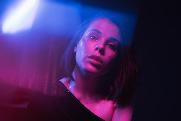 Fashionable female portrait with blue highlights in neon purple light posing for the camera