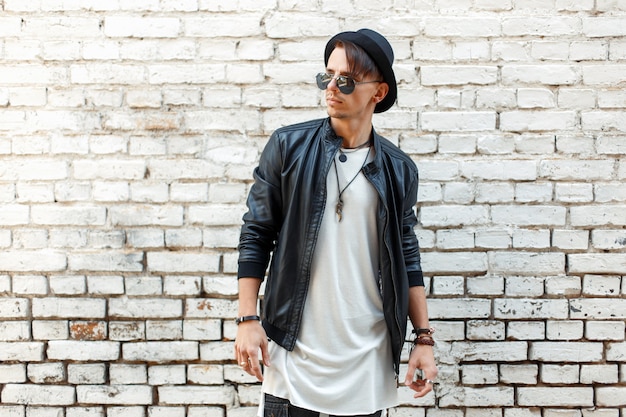 Fashionable handsome man in stylish clothes posing near an old white brick wall