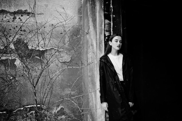 Fashionable long legs brunette model in long black cloak posed outdoor at winter day against old grunge wall.