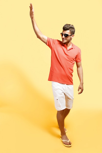 Fashionable man saluting walking against yellow 