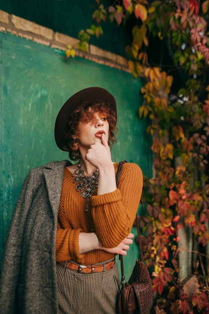 Fashionable portrait of stylish lady in vintage clothing and hat and rustic background looking away