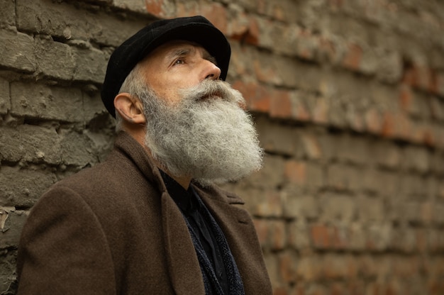 Fashionable senior man with gray hair and beard is outdoors on the street.