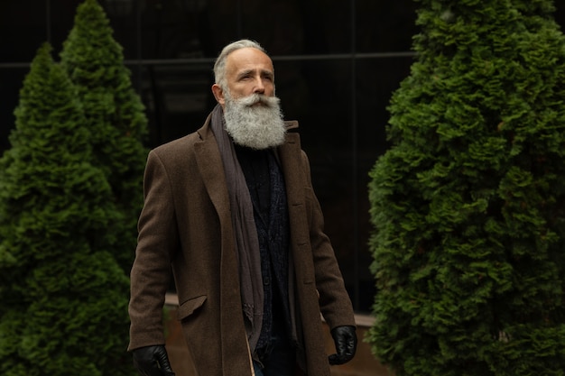 Fashionable senior man with gray hair and beard is outdoors on the street.