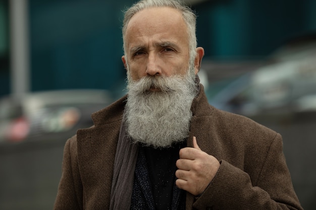 Fashionable senior man with gray hair and beard is outdoors on the street.