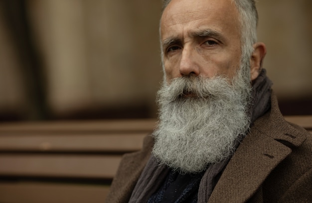 Fashionable senior man with gray hair and beard is outdoors on the street.