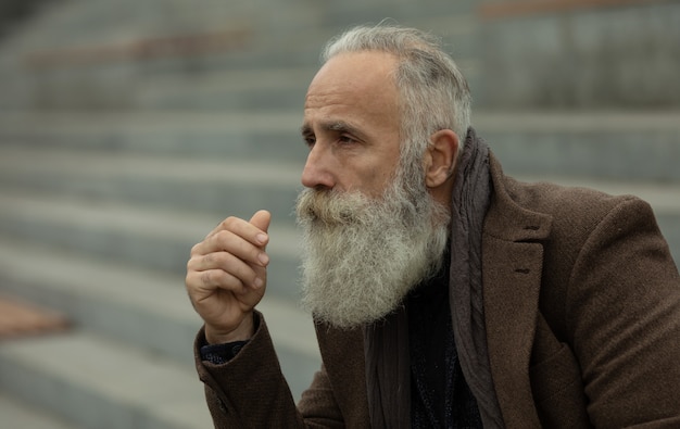 Fashionable senior man with gray hair and beard is outdoors on the street.