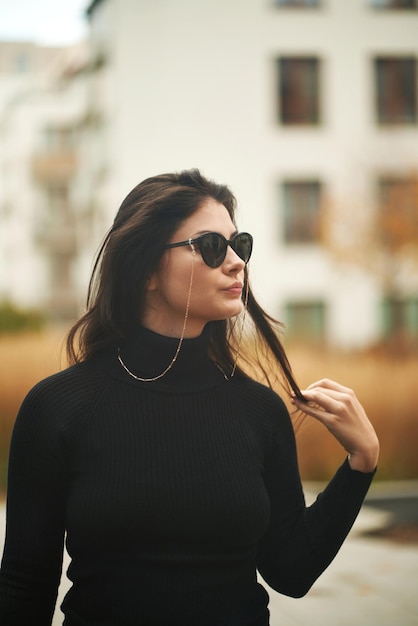 Fashionable and sexy portrait of a brunette woman The confident and trendy young girl wears sunglasses and chains Woman with long natural dark hair