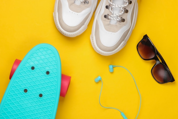 Fashionable sneakers with cruiser board, sunglasses, earphones on yellow. Youth fun